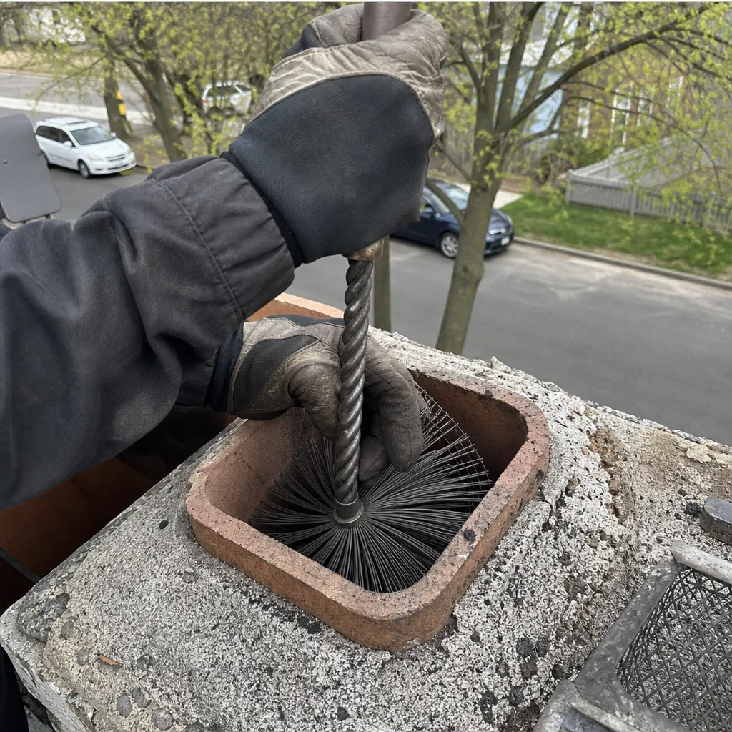 Professional chimney sweep cleaning a chimney flue with a wire brush.